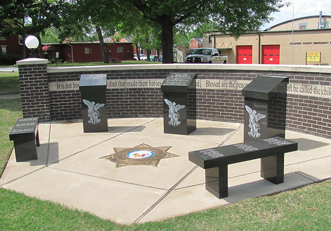 Engraved monuments with bench and brick wall on concrete platform with star shield in its center