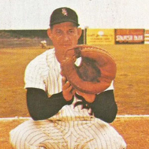 White man in baseball uniform crouching with glove on field