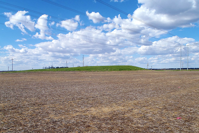 Mound of earth with flat land around it under blue skies