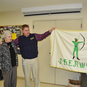 White man and old white woman looking at Sherwood flag with green-clad archer on white field