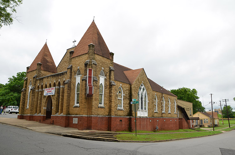 Brick church building with twin front towers and stained glass windows on street corner