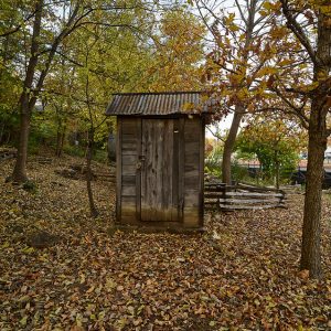 Wooden outhouse in wooded area with wooden fence behind it