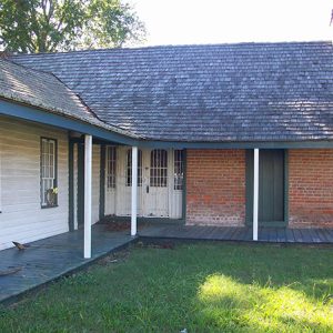 Side view of single-story brick house with covered L-shaped porch on grass