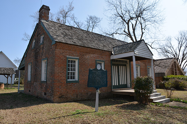 Single-story brick house with covered porch and historical marker sign in front yard