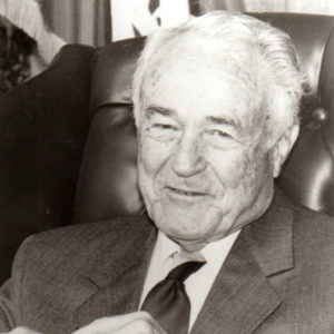 Old white man smiling in suit and tie seated in leather chair