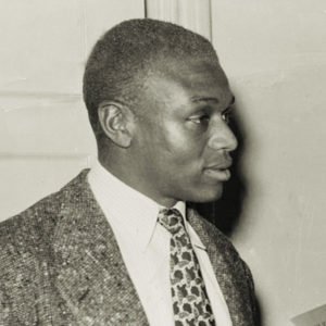 Black man in woven suit jacket pattern tie by doorway profile view