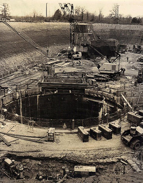 Massive circular hole in the earth surrounded by cranes and other items of construction equipment
