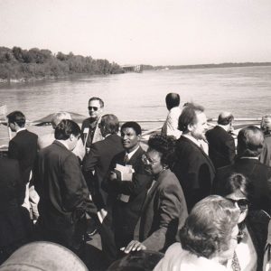 mixed group of people, many in suits or dresses, on boat in middle of river