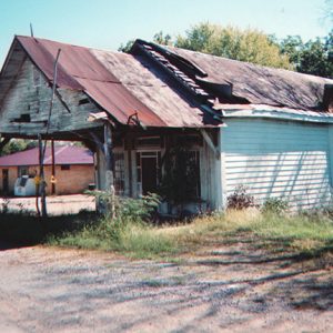 Run-down single-story building with covered porch on dirt road