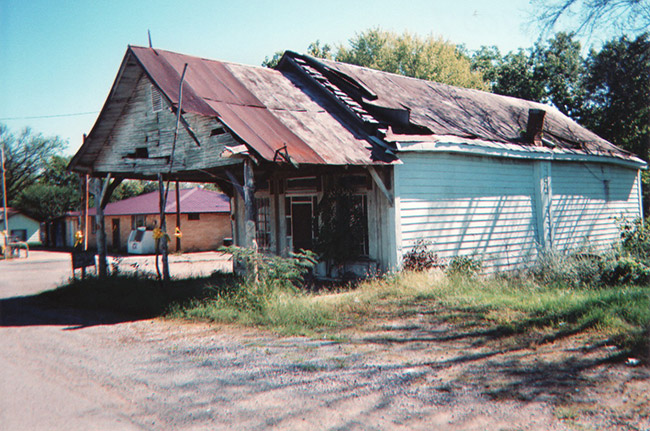 Run-down single-story building with covered porch on dirt road
