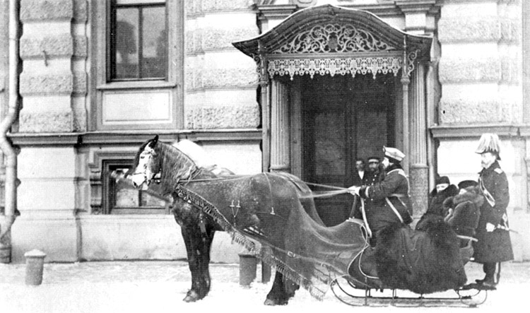White woman and men in uniform on horse drawn sleigh outside  multistory building