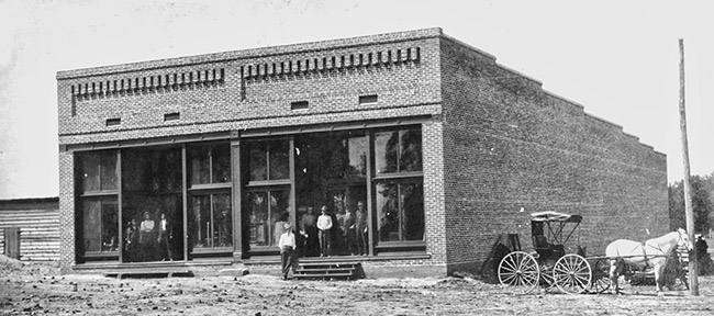 Brick storefront with large windows on dirt road