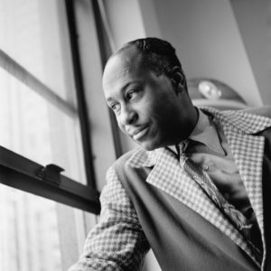 African-American man in plaid suit jacket and tie looking out a window