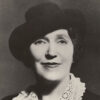 White woman smiling in hat and dress with lace collar