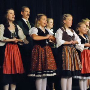 White man in suit with white woman and girls in dresses singing