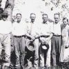Group of white men and a woman and a girl standing together under a tree