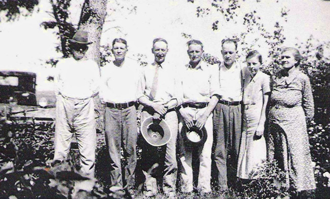Group of white men and a woman and a girl standing together under a tree