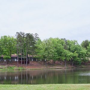Large cabin building surrounded by trees as seen from opposite a lake