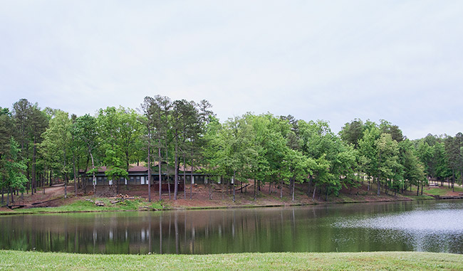 Large cabin building surrounded by trees as seen from opposite a lake