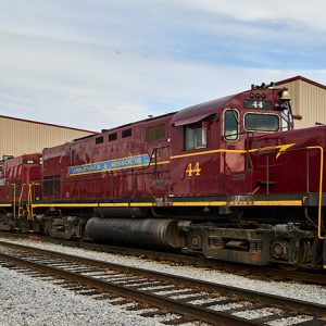 Red diesel locomotives on tracks outside of building with flat roof