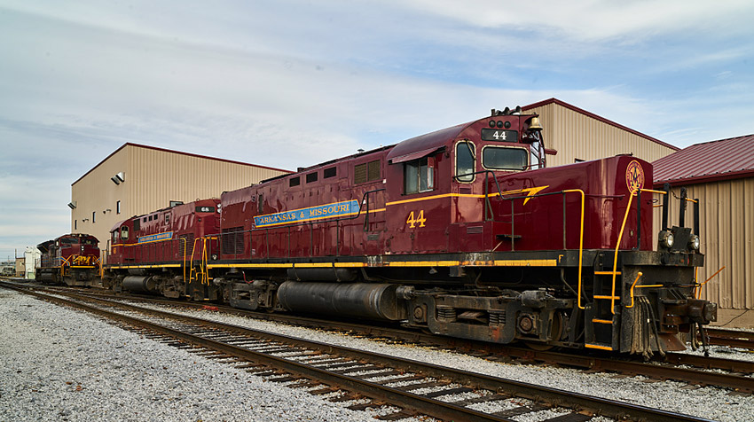 Red diesel locomotives on tracks outside of building with flat roof