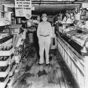 White man standing in store with glass cases and wooden floors