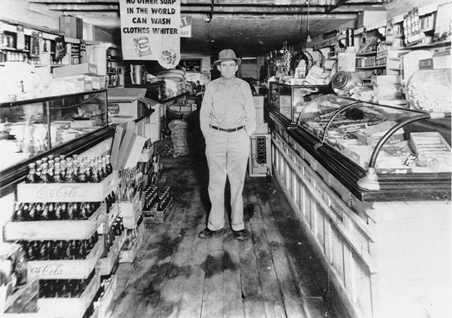 White man standing in store with glass cases and wooden floors