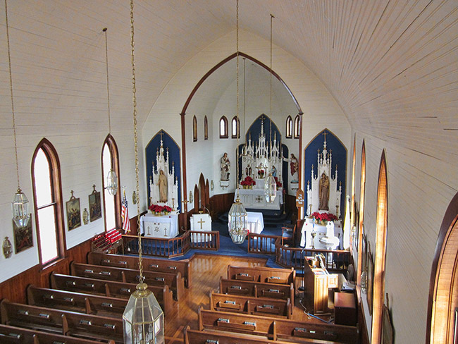 Wooden pews and high altar section in sanctuary room with hanging light fixtures and gothic arch windows