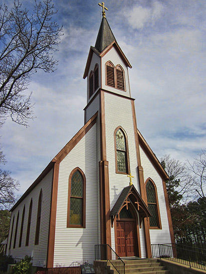 white building with darker wood trim with tall steeple tower and cross on top