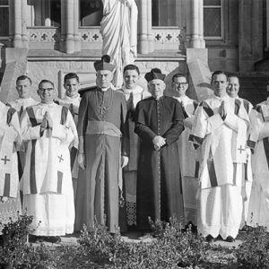 Group of white men in religious garb with statue behind them