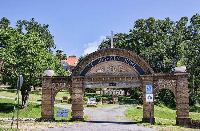 Brick arch over driveway with cross on top and "St. Joseph's Home" written on center portion