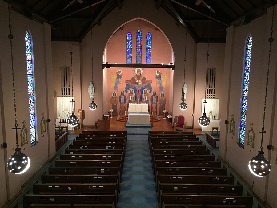 Interior of church sanctuary with rows of pews and painting of a crucified Jesus and angels behind the altar