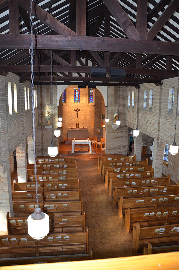Interior of brick church sanctuary with wooden pews looking towards the altar from above