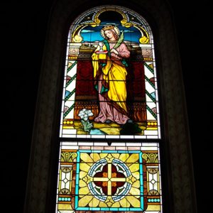 Arched stained glass window featuring white woman in robes with crown and chalice on