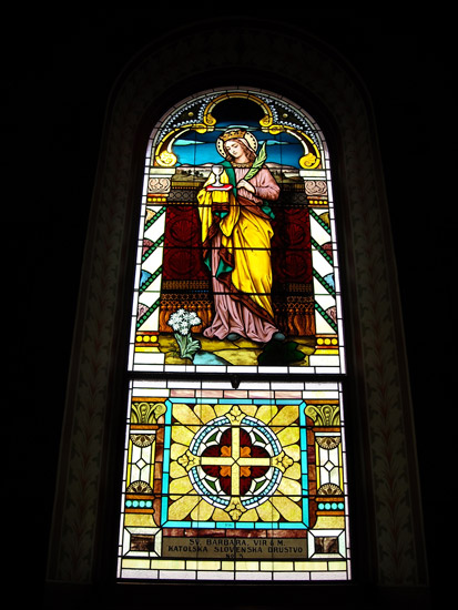 Arched stained glass window featuring white woman in robes with crown and chalice on