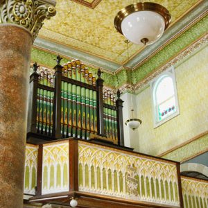 Ornate pipe organ with detailed balcony supported by columns inside multistory building with hanging light fixtures