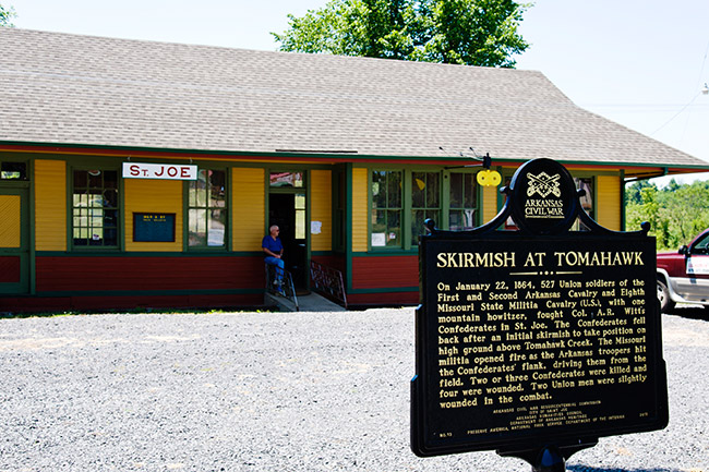 Red yellow and green building with "Skirmish at Tomahawk" historical marker sign in front of it