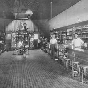 Four men in dark pants, white shirts, and suspenders in drug store