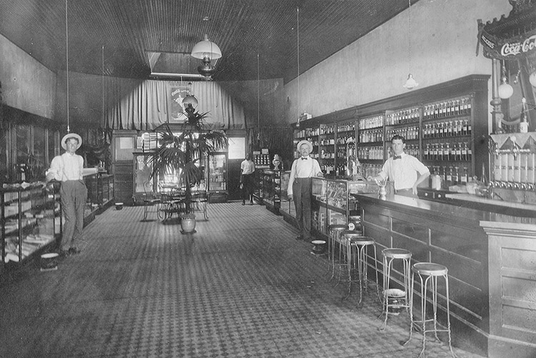 Four men in dark pants, white shirts, and suspenders in drug store