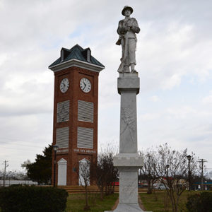 Stone monument featuring soldier on pedestal with clock tower in the background