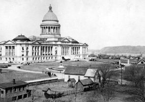 Large marble building with dome and formal grounds surrounded by trees and smaller wooden buildings
