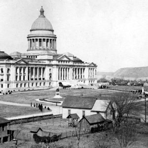 Large marble building with dome and formal grounds surrounded by trees and smaller wooden buildings