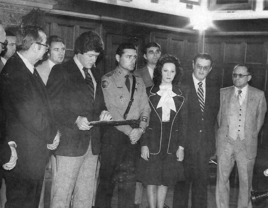 White man in suit giving an award to white man in police uniform with white men in suits and white woman standing with them