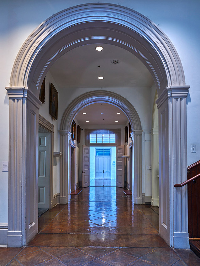 Looking down hallway with open doors and arches over tiled floor