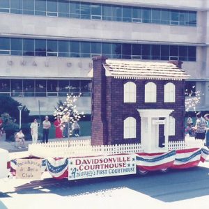 Miniature multistory brick building and fence on parade float in front of multistory building