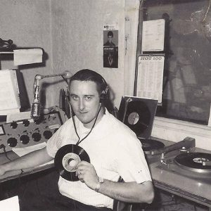 White man holding a vinyl record sitting in radio control room