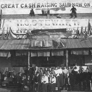 Group of people standing in front of store topped with banner "Great Cash Raising Sale Now On"