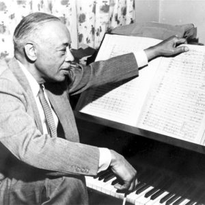 African-American man in suit and tie at piano composing music