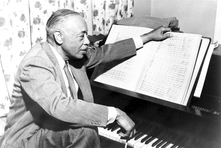 African-American man in suit and tie at piano composing music