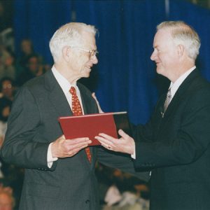 White man in suit hand an award to older white man in suit